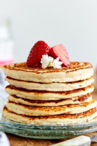 A stack of six protein pancakes on a plate with a sliced strawberry on top.