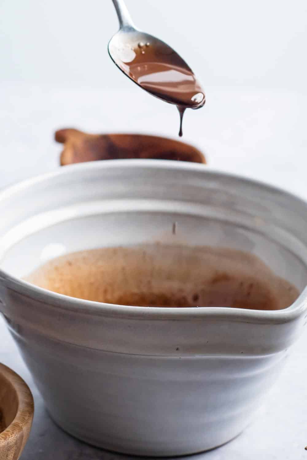 A spoon with melted chocolate on it over a bowl.