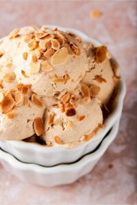 A bunch of scoops of almond ice cream on top of one another in a white bowl.