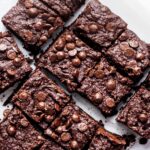 Four rows of three squares of brownies on a piece of parchment paper.