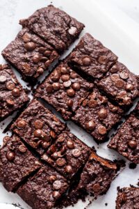 Four rows of three squares of brownies on a piece of parchment paper.