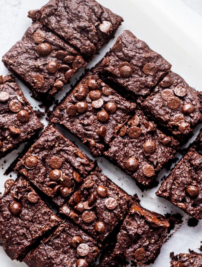 Four rows of three squares of brownies on a piece of parchment paper.