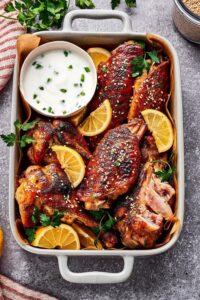 A bunch of turkey wings in a casserole dish with a cup of dipping sauce in it.