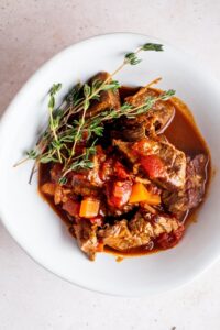 A few tomatoes and carrots on top of carne picada that is in a sauce in a white bowl.