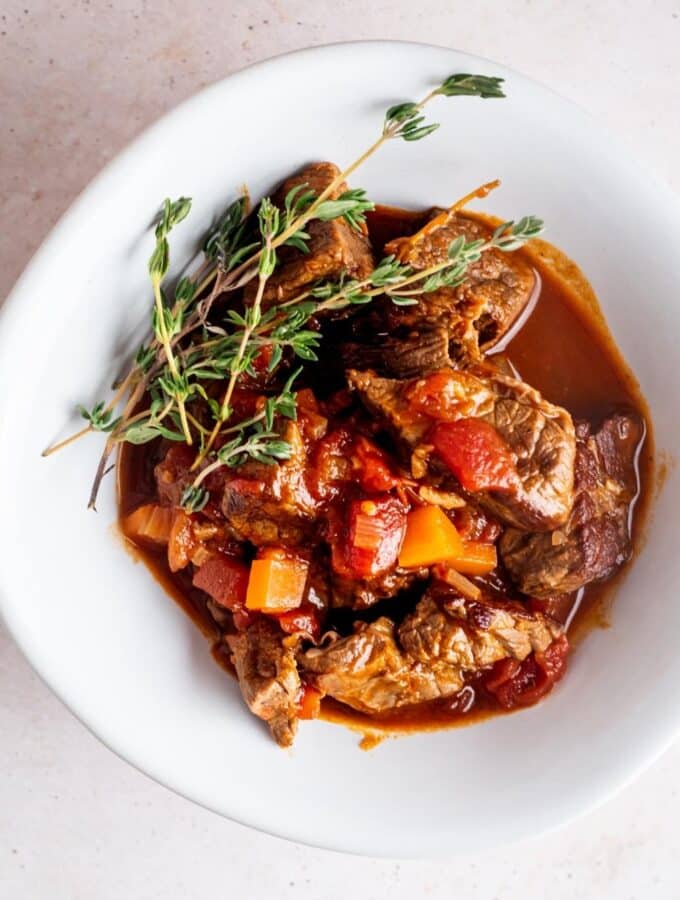 A few tomatoes and carrots on top of carne picada that is in a sauce in a white bowl.