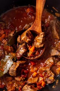 A wooden ladle with Carne picada meat in it and a Dutch oven filled with Carne picada.