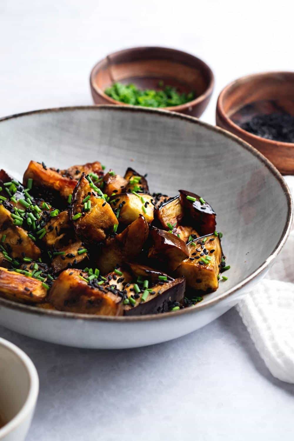 Part of a white bowl that is filled with eggplant squares.