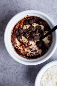 Chocolate chips in cocoa powder on top of protein overnight oats in a white bowl.