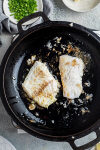 Two mahi mahi fillets cooking in a skillet.