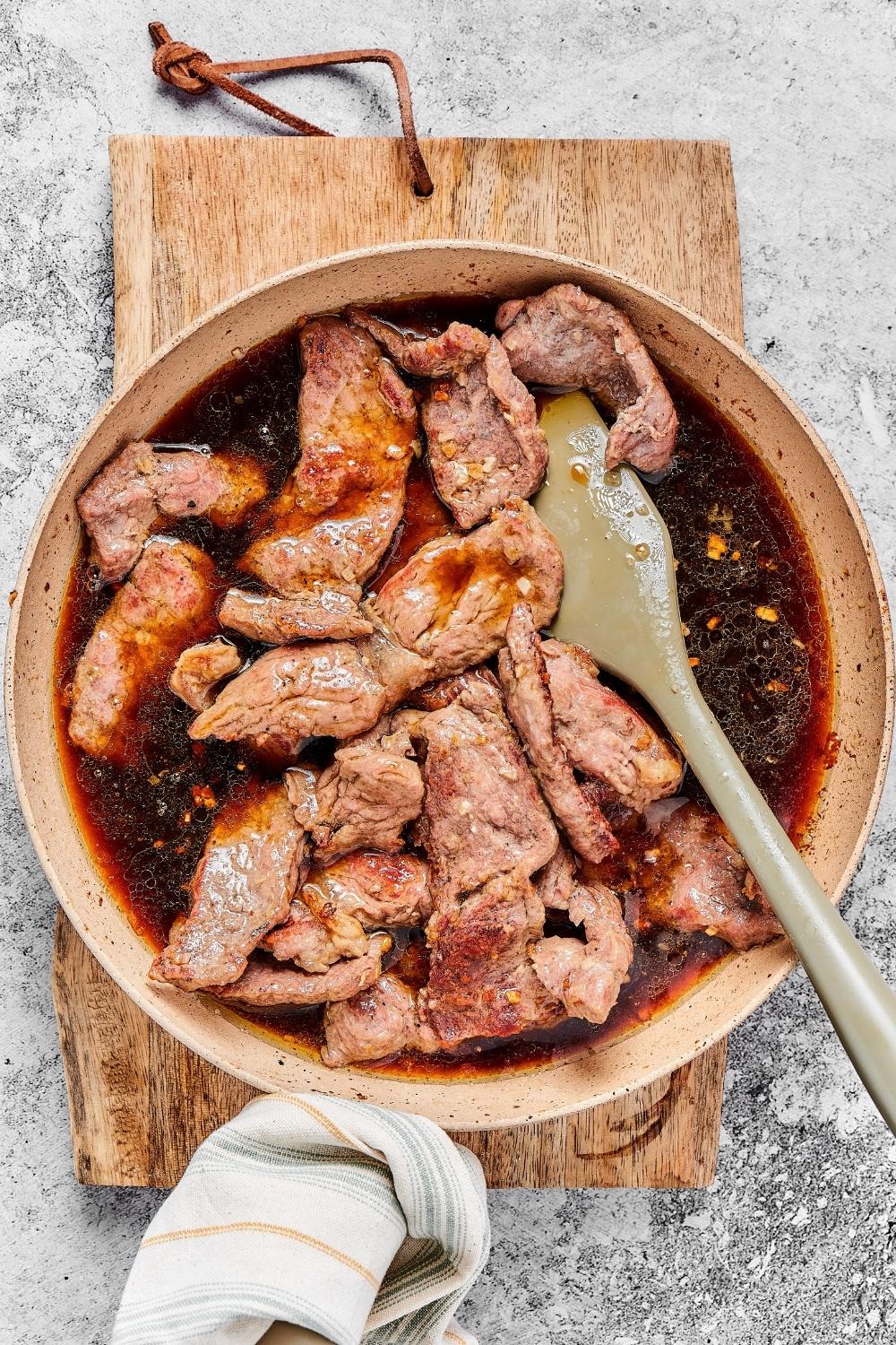 A bowl of stir fry sauce and beef on a wooden cutting board.