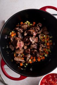 Carne picada on top of chopped celery, carrots, and onion in a Dutch oven.