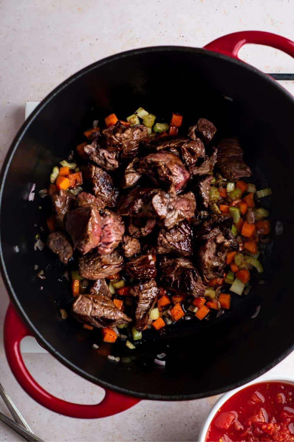 Carne picada on top of chopped celery, carrots, and onion in a Dutch oven.