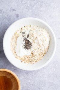 Chia seeds on top of yogurt on top of vanilla protein powder and oats in a white bowl on a grey counter.
