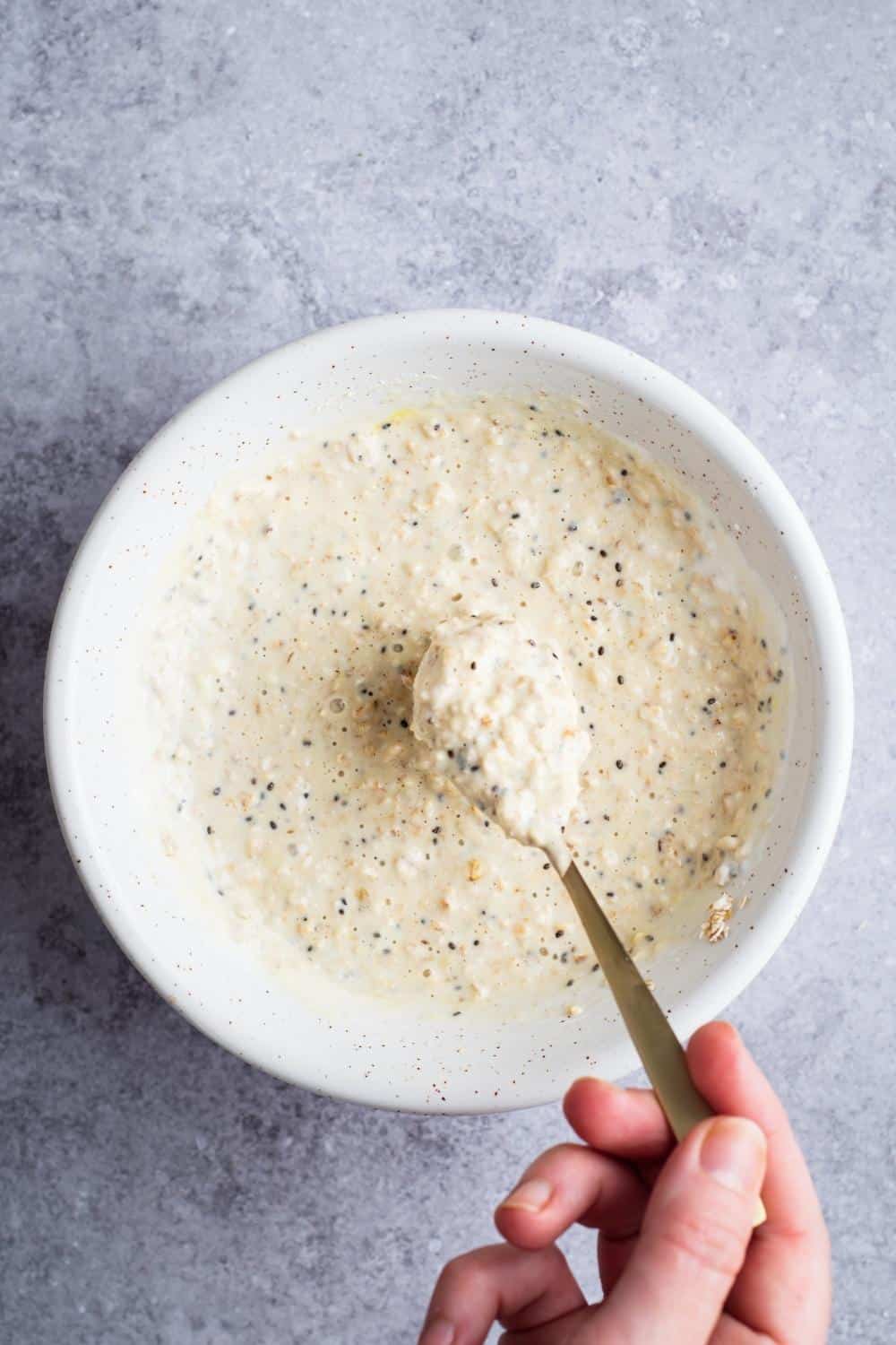 A hand holding a spoon protein overnight oats on it right above a ball that is filled with overnight oats.