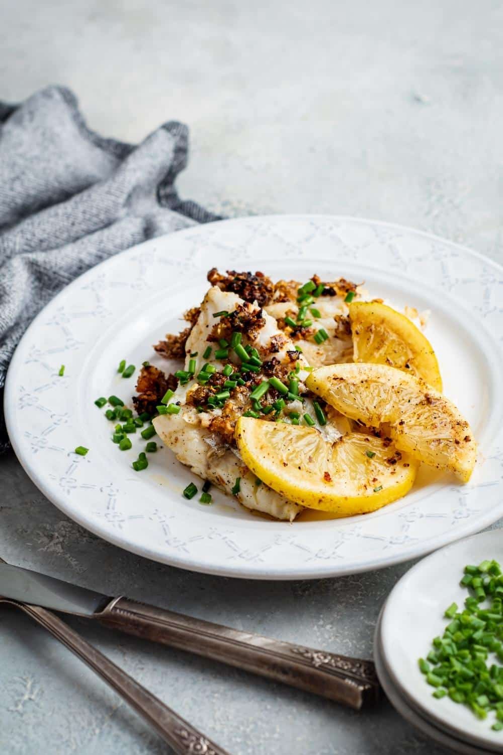 A plate with mahi mahi fillets and lemon wedges on it.