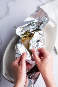 Two hands folding up tin foil around sea bream.