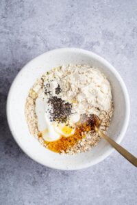 Chia seeds, yogurt, honey, protein powder, and rolled oats in a white bowl on top of a gray counter.