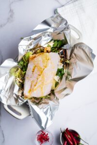 A fillet of snapper on top of greens in tin foil in a casserole dish.