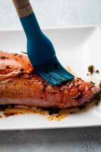 A brush rubbing seasoning on part of turkey tenderloin.