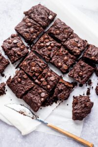 Four rows of four brownies on a piece of parchment paper.