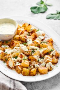 An oval plate with yogurt dressing covered roasted kohlrabi and a bowl of the dressing on it.