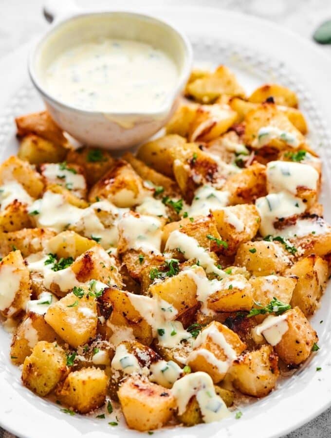 Roasted kohlrabi with yogurt dressing on top of with a bowl of the yogurt dressing on the plate.