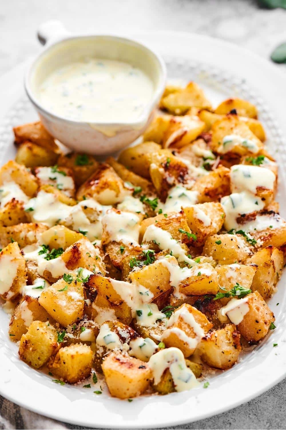 Roasted kohlrabi with yogurt dressing on top of with a bowl of the yogurt dressing on the plate.