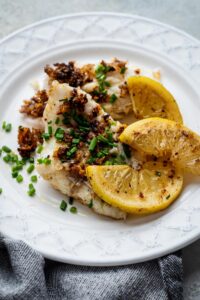 Lemon wedges and two mahi mahi fillets on a plate.