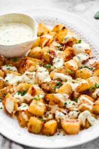 A white plate that has a bowl of yogurt dressing and a bunch of squares of roasted kohlrabi with the dressing on top.