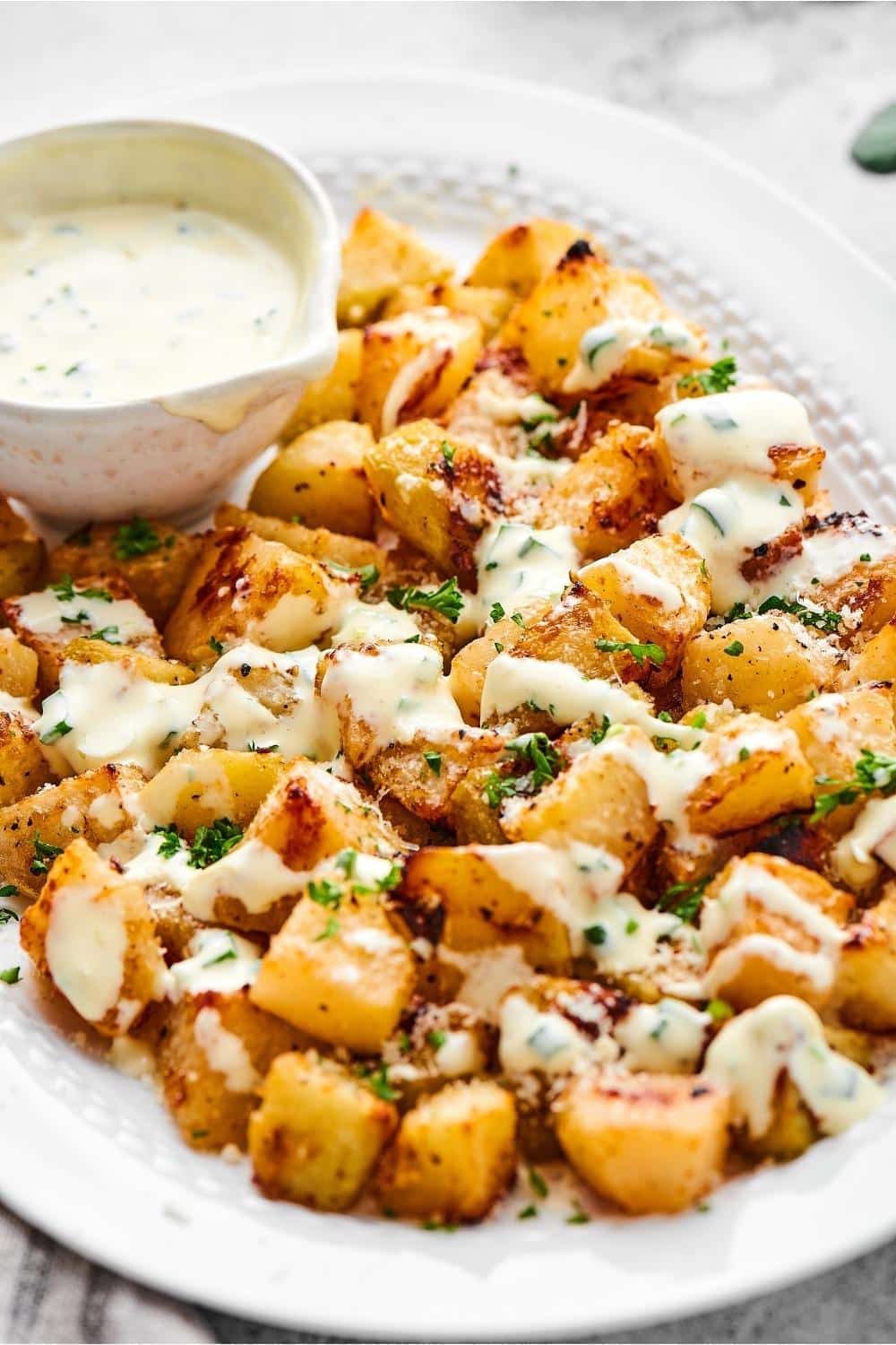 A white plate that has a bowl of yogurt dressing and a bunch of squares of roasted kohlrabi with the dressing on top.