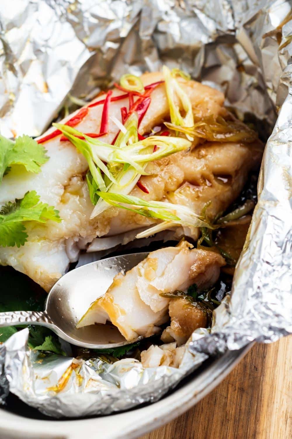 A spoon with a piece of sea bream on it in front of a sea bream fillet in tin foil.