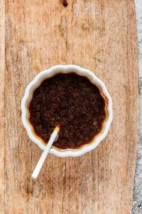 A white bowl filled with soy sauce on a wooden cutting board.