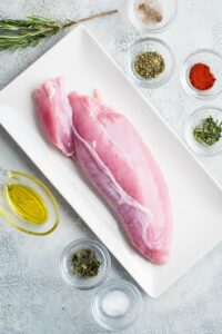 Turkey tenderloin on a white plate surrounded by a bunch of glass bowls of seasoning.