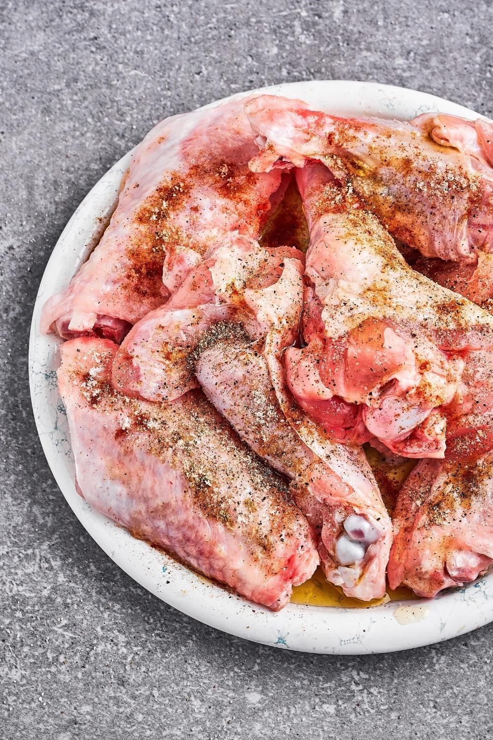 Seasoned raw turkey wings on a white plate.