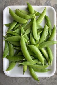 Sugar snap peas on a white plate.