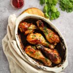 An overhead view of six baked chicken legs in a white casserole dish.