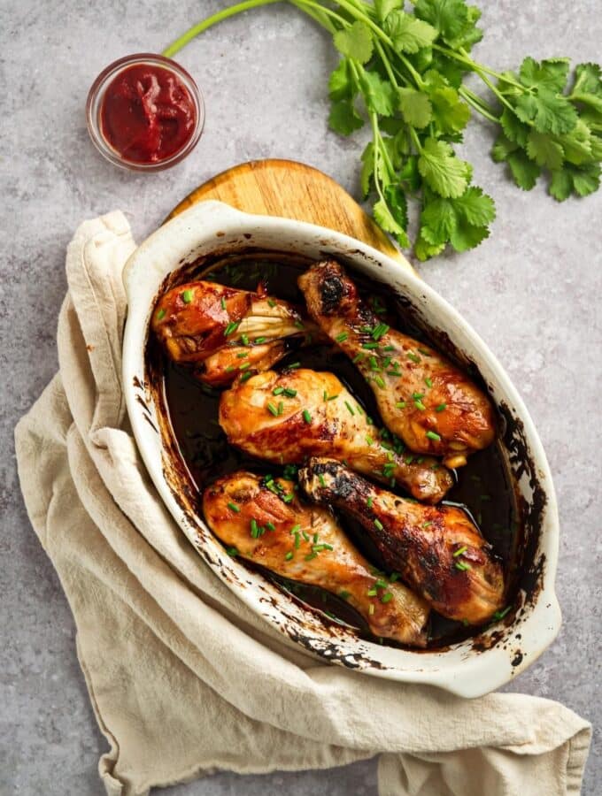 An overhead view of six baked chicken legs in a white casserole dish.