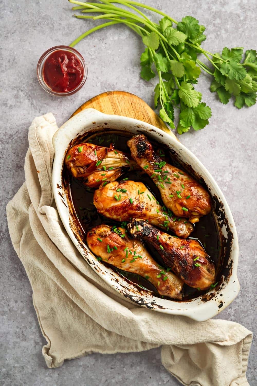 An overhead view of six baked chicken legs in a white casserole dish.