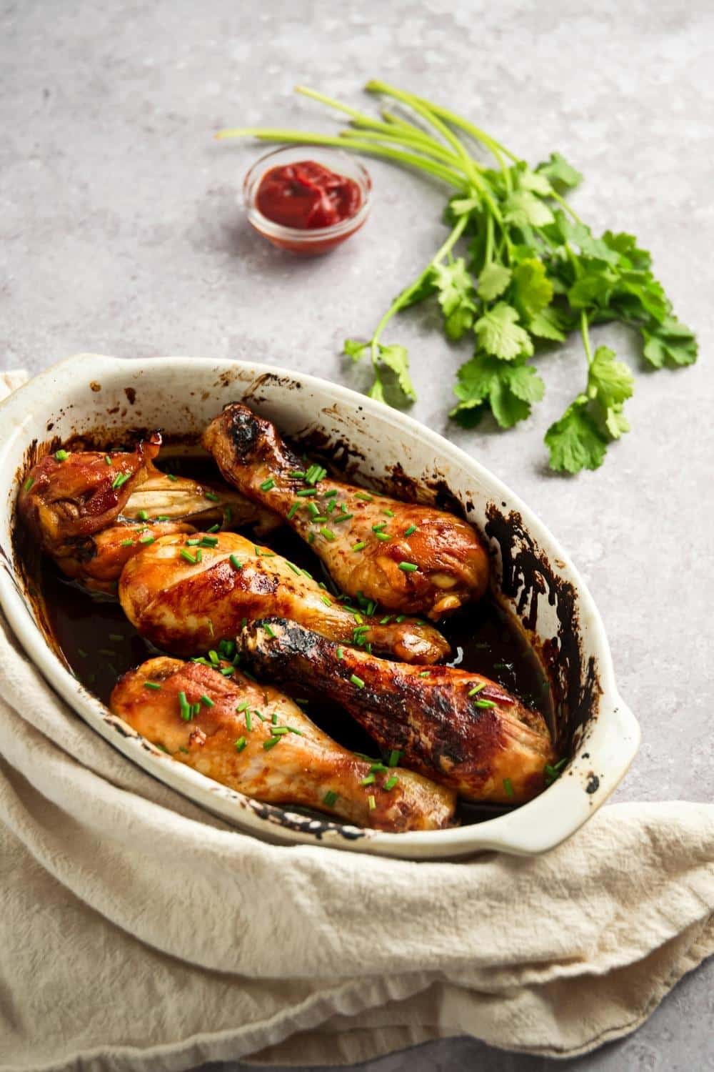 Six baked chicken legs in a white casserole dish.