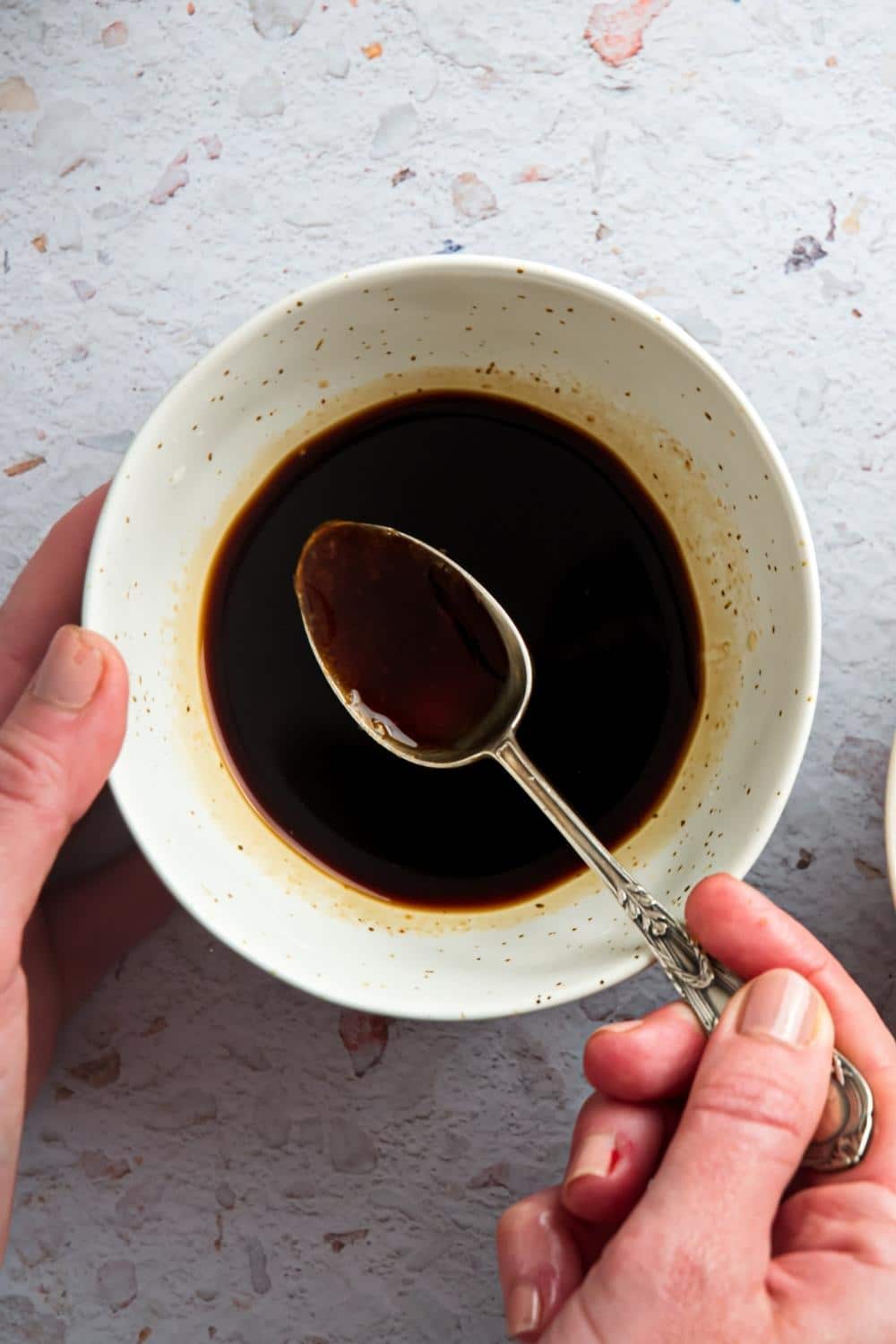 A hand holding a spoon with sauce in it over a bowl of sauce.