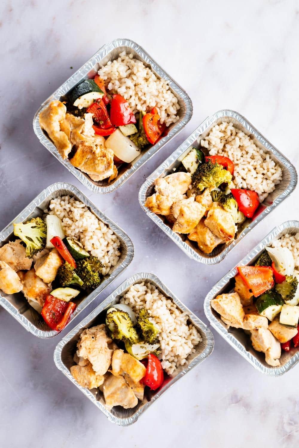 Chicken, veggies, and rice in five individual containers on a grey counter.