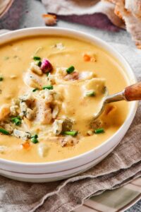 A spoon scooping some buffalo chicken soup out of a white bowl filled with the soup.