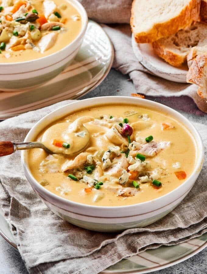 A bowl of buffalo chicken soup with a spoon in it. Behind it is part of another bowl of soup and some slices of white bread.