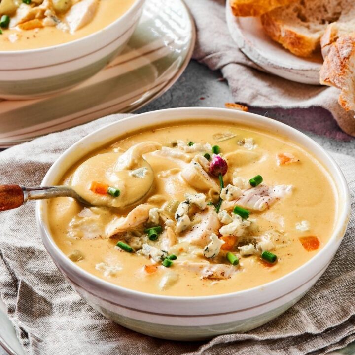 A bowl of buffalo chicken soup with a spoon in it. Behind it is part of another bowl of soup and some slices of white bread.