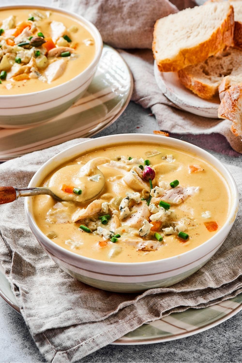 A bowl of buffalo chicken soup with a spoon in it. Behind it is part of another bowl of soup and some slices of white bread.