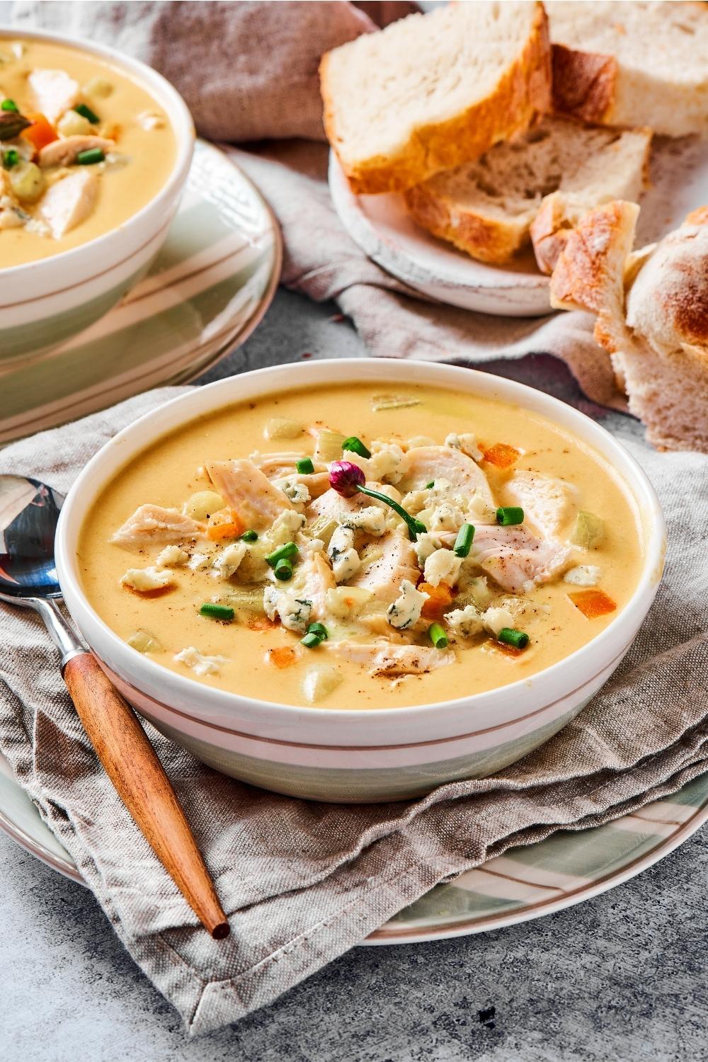 A white bowl filled with buffalo chicken soup with a spoon next to it on a tablecloth on a plate on a counter.