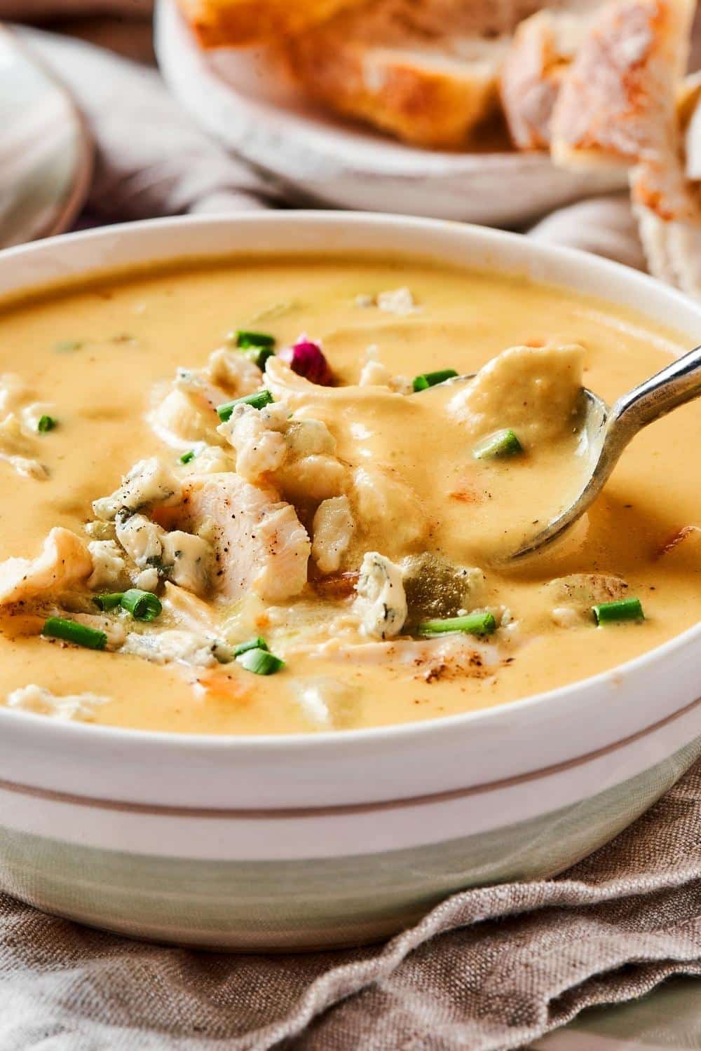 A spoon scooping some buffalo chicken soup form a bowl filled of buffalo chicken soup.