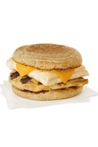 A sliced english muffins with cheese, a folded egg white, and grilled chicken between it.