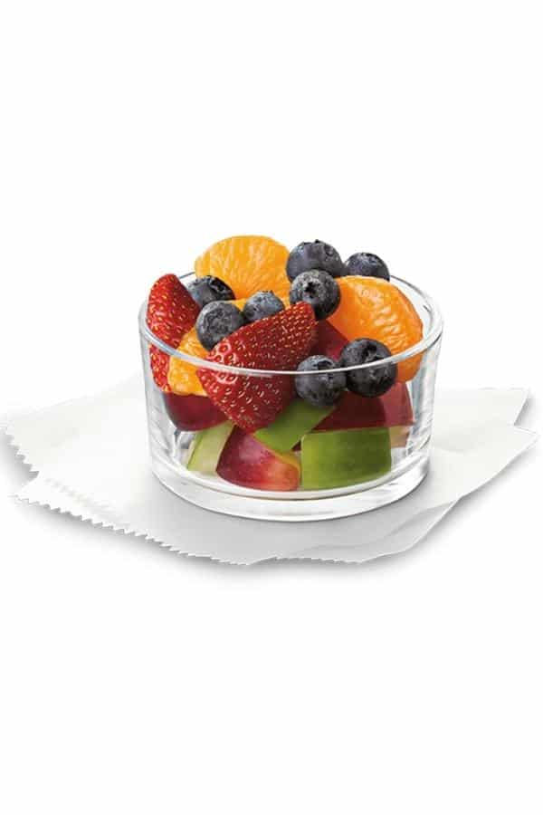 A glass cup filled with strawberries, blueberries, mandarin oranges, and apple slices.