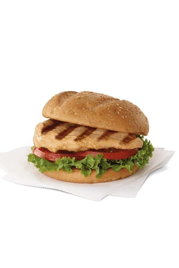 A sliced bun with grilled chicken, tomato, and lettuce between it.